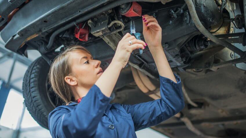 Photo of young female mechanic inspecting a CV join on a car in auto repair shop.