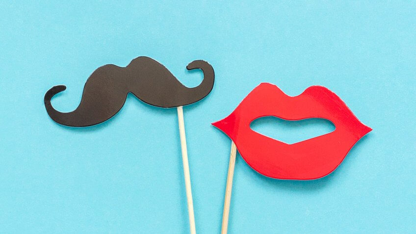Couple paper mustache and lips props on stick in ice cream waffle cone on blue background.