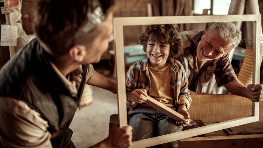 Close up of a boy learning how carpenting works from his father and grandfather.