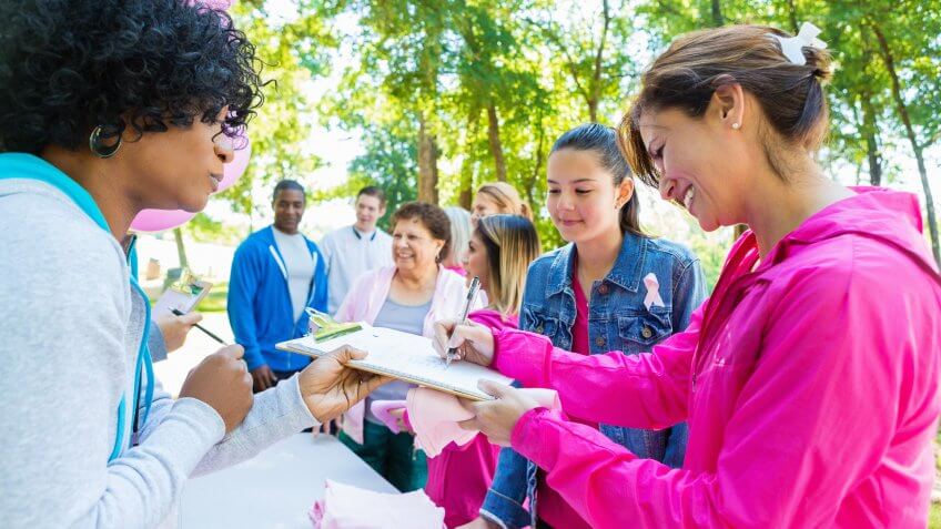 Diverse group of adults and teenagers are lined up at registration table in sunny park.