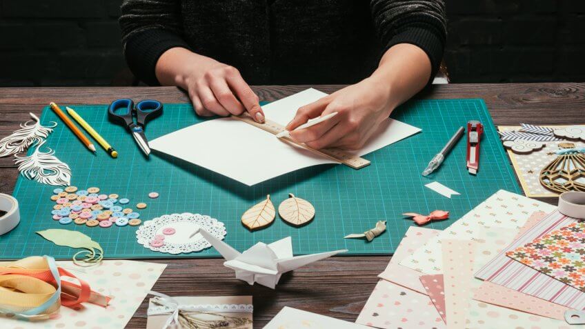 cropped image of designer cutting paper for scrapbooking greeting postcards.