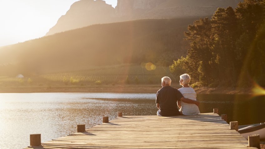 Romantic Senior Couple Sitting On Wooden Jetty By Lake.