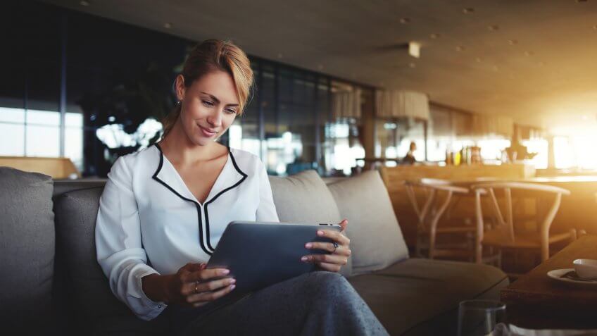 Female financier is reading financial news in internet via touch pad during work break in modern cafe.