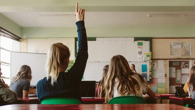 Rear view of female student sitting in the class and raising hand up to ask question during lecture.