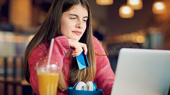 A teenage girl is shopping online with her credit card in a coffee shop.