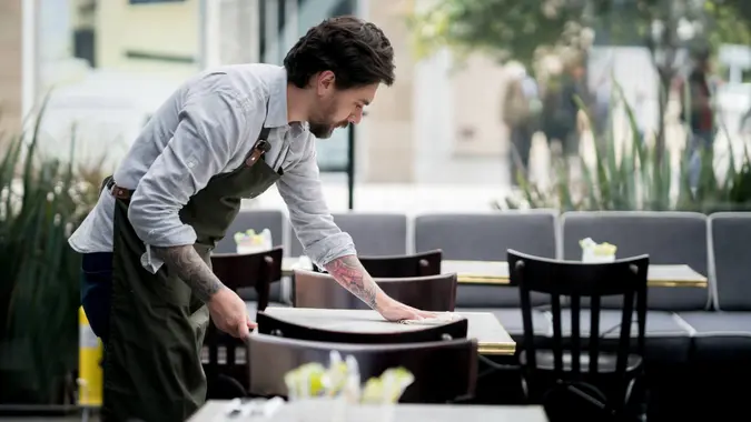 Happy waiter cleaning the tables at a restaurant - food service occupation.