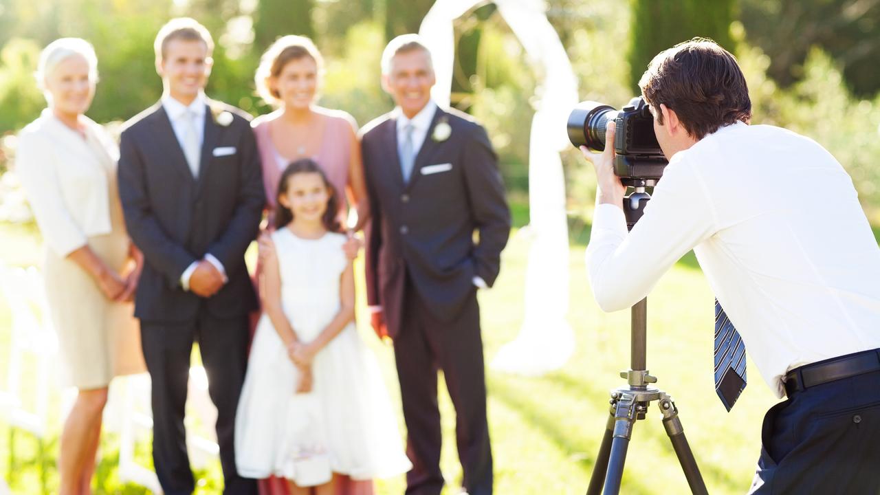 Young man photographing family at outdoor wedding.