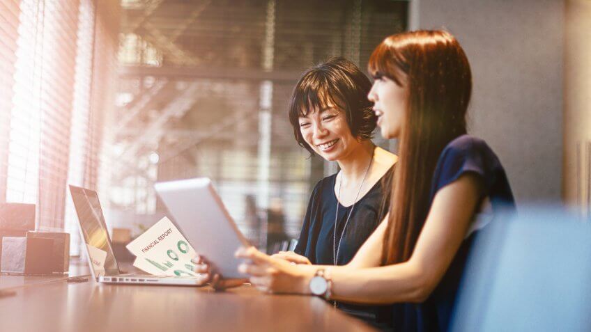 Two young Japanese businesswomen discuss options for investment and other development projects in modern office.
