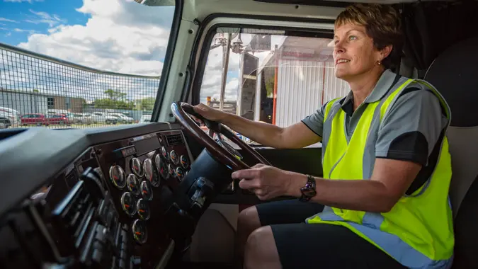 Empowered happy woman driving a truck in the transport industry wearing high visibility clothing.