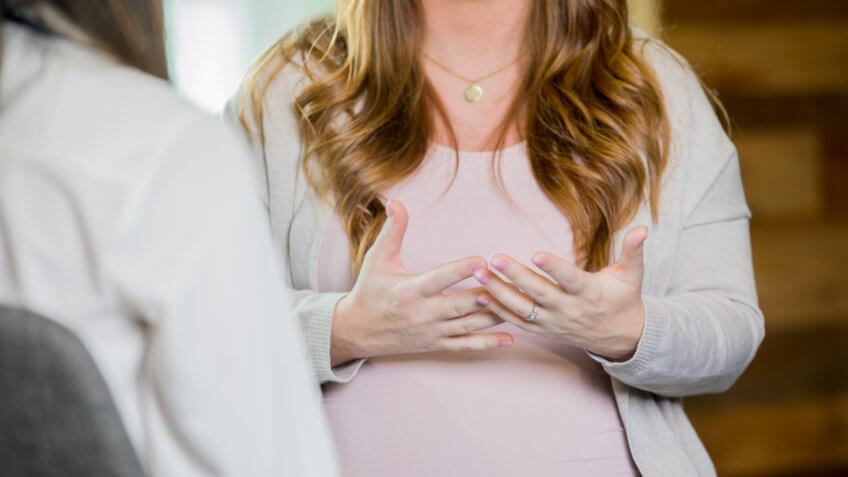 Mid adult Caucasian unrecognizable woman is attending a pregnancy support group meeting or childbirth class, and is discussing something.
