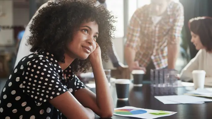 Shot of a young female designer looking thoughtful while sitting at a conference table with her colleagues.