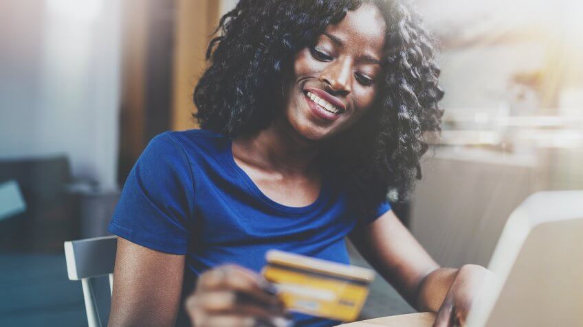 Woman shopping online through laptop using credit card at home.