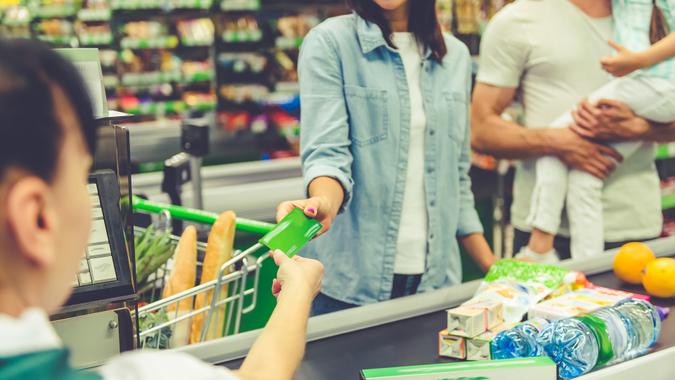 Cropped image of beautiful young parents and their little daughter standing near cash desk in the supermarket.