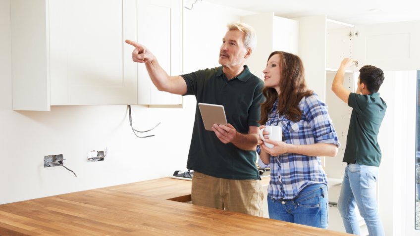 Woman With Carpenter Looking At Plans For Kitchen On Digital Tablet.