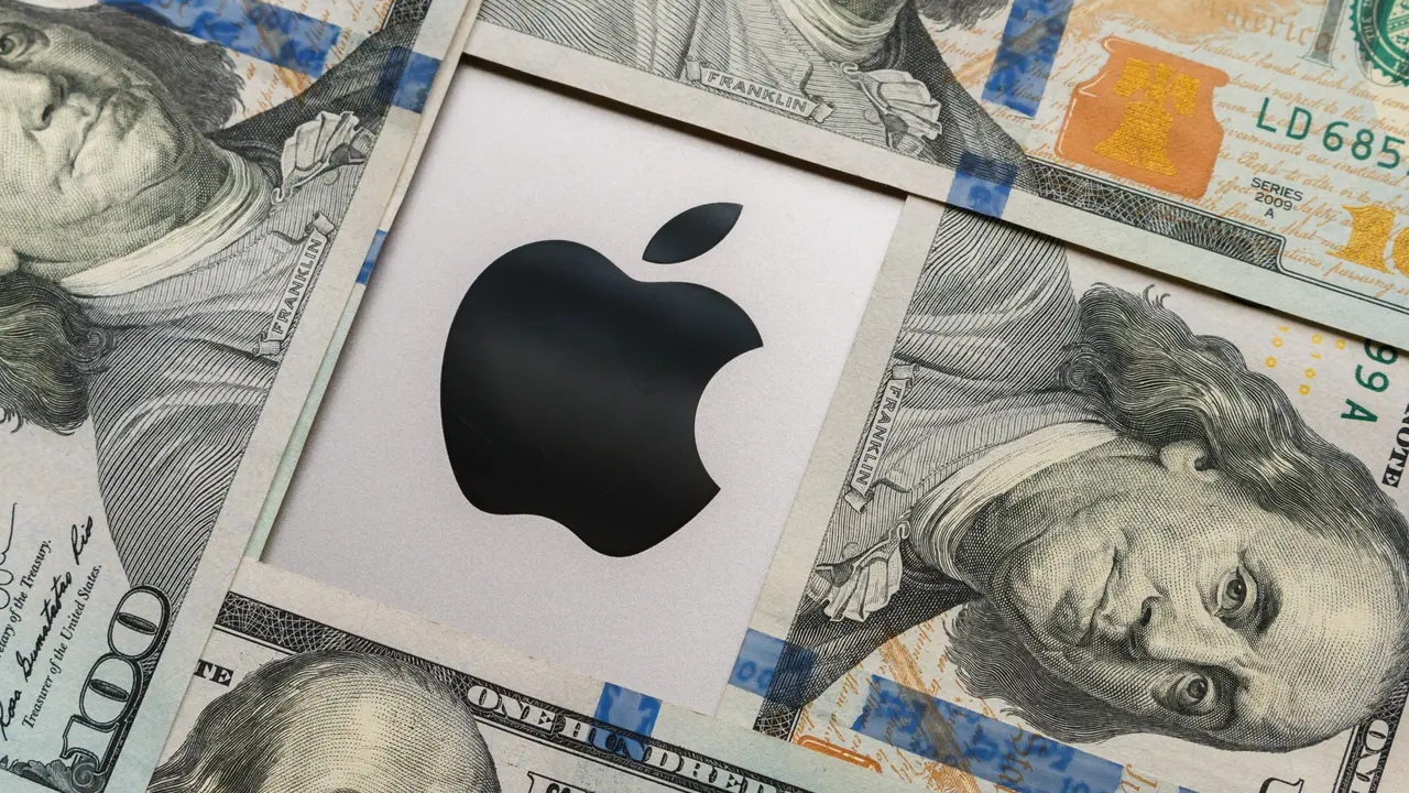 Close-up of an Apple logo resting on a neat pile of 100-dollar bills, with the bills' details clearly visible.