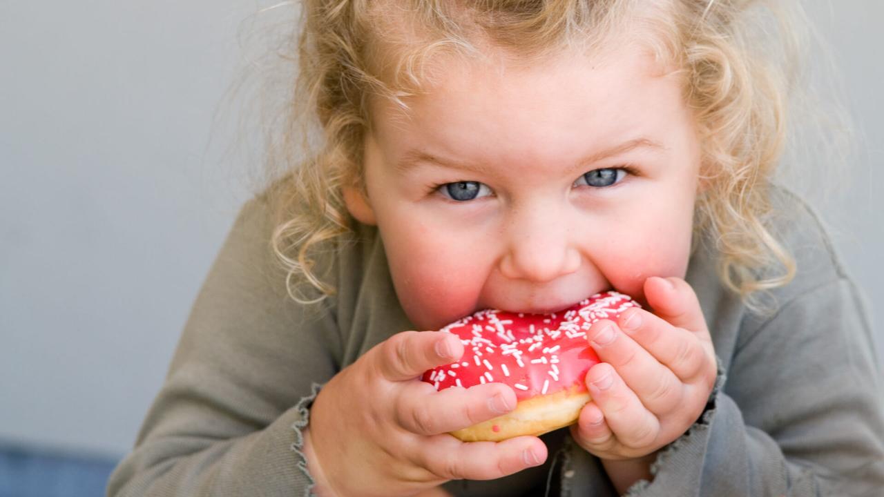 Young girl aged 2 to 3 years eating donut with pink icing.