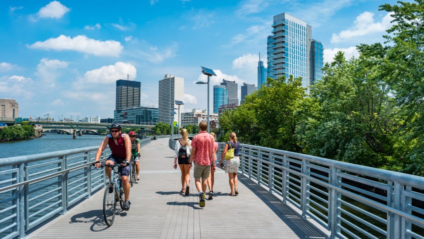 People bike and walk on the Schuylkill Banks Boardwalk in downtown Philadelphia, Pennsylvania, USA on a sunny summer day.