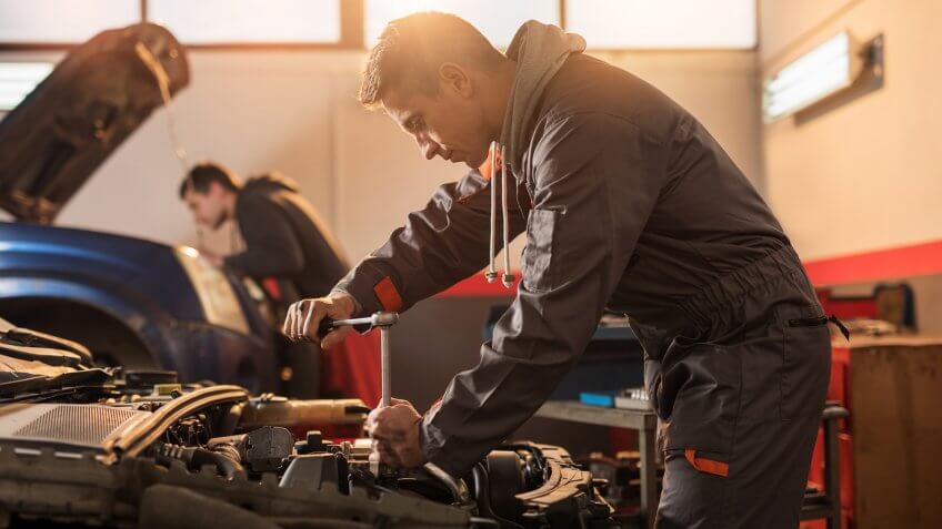 Mid adult mechanic repairing a car in auto repair shop.