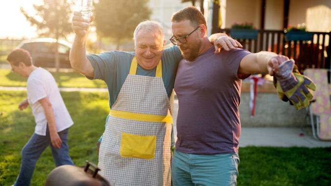 baby boomer father and millennial son barbecuing in backyard