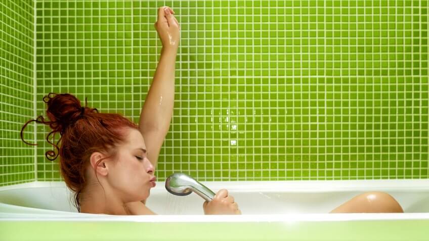 side view of woman in bathtub singing, enjoying bath and having fun.