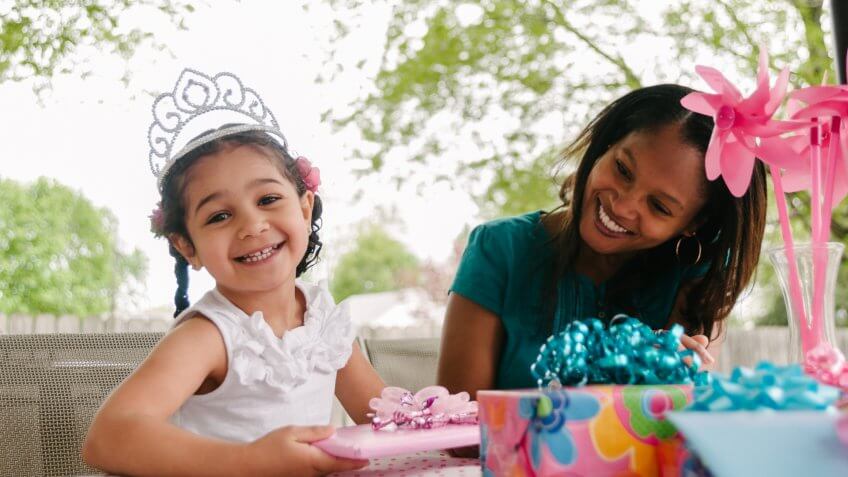 Girl princess tiara opening her gifts with her mother at her birthday party.