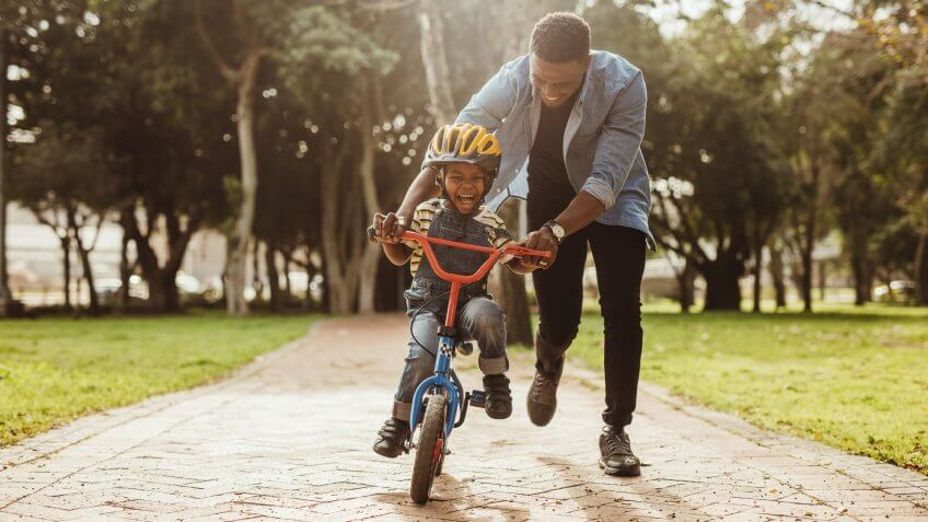 Boy learning to ride a bicycle with his father in park.