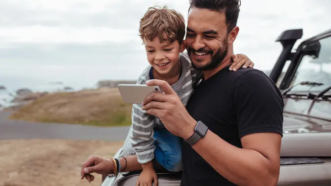 Father with little boy using smart phone together during road trip.