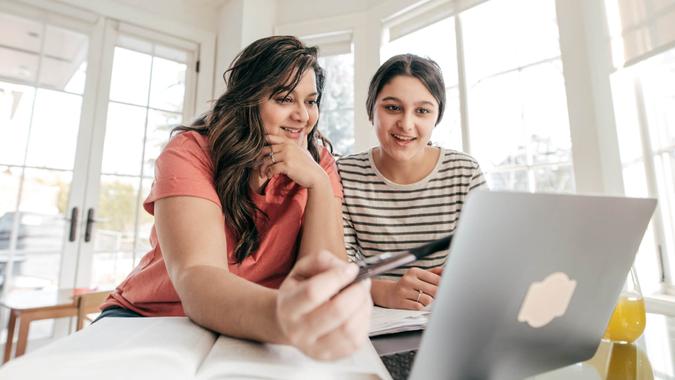 mother and teenage daughter looking at college costs on laptop