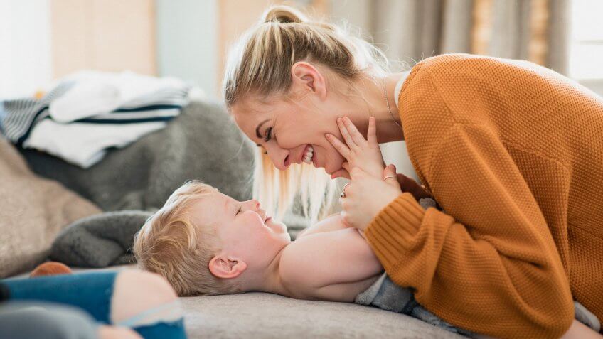 Mother cuddling with young son as he lays on the sofa in front of her.