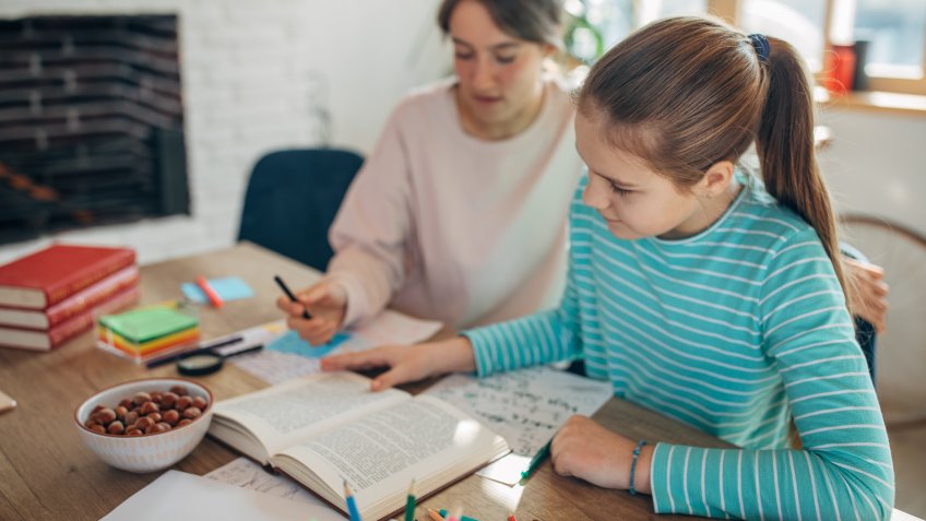 Private teacher helping teenage girl doing homework.