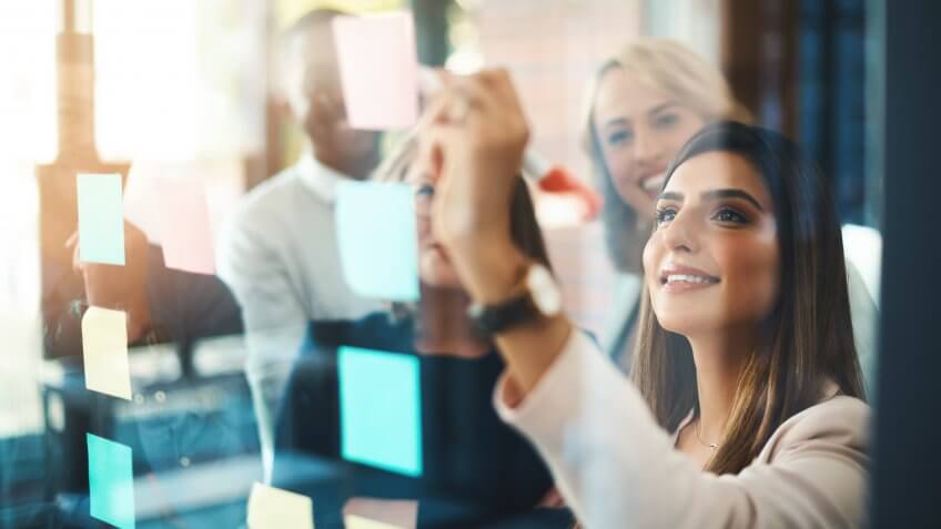 Shot of a group of businesspeople arranging sticky notes on a glass wall in a modern office.