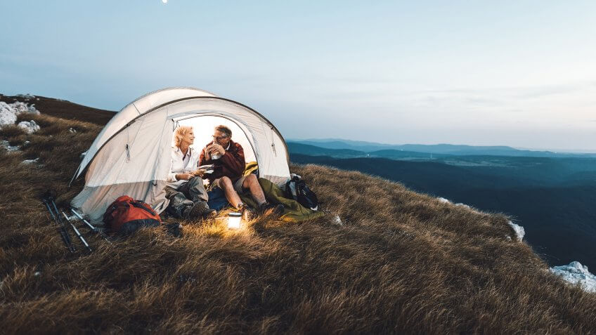 Senior couple camping in the mountains and eating a snack.