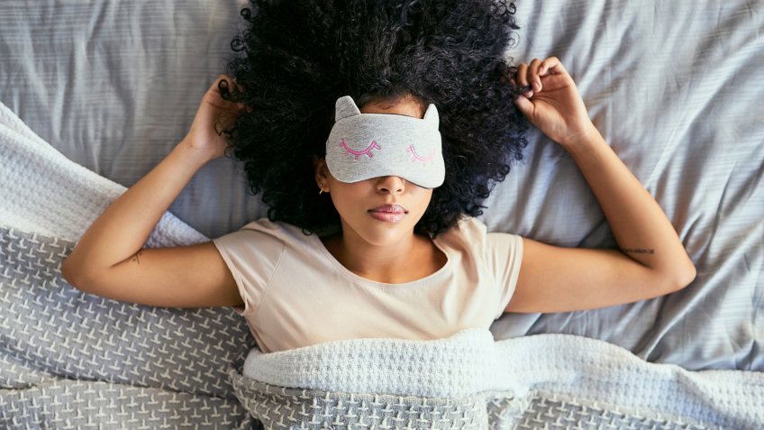 Shot of a young woman sleeping with a mask on in bed.