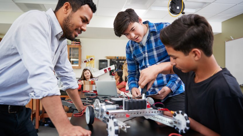 Teacher With Male Pupils Building Robotic Vehicle In Science Lesson.