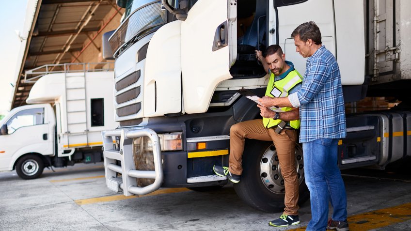 Shot of two coworkers talking together next to a large truck outside of a distribution center.