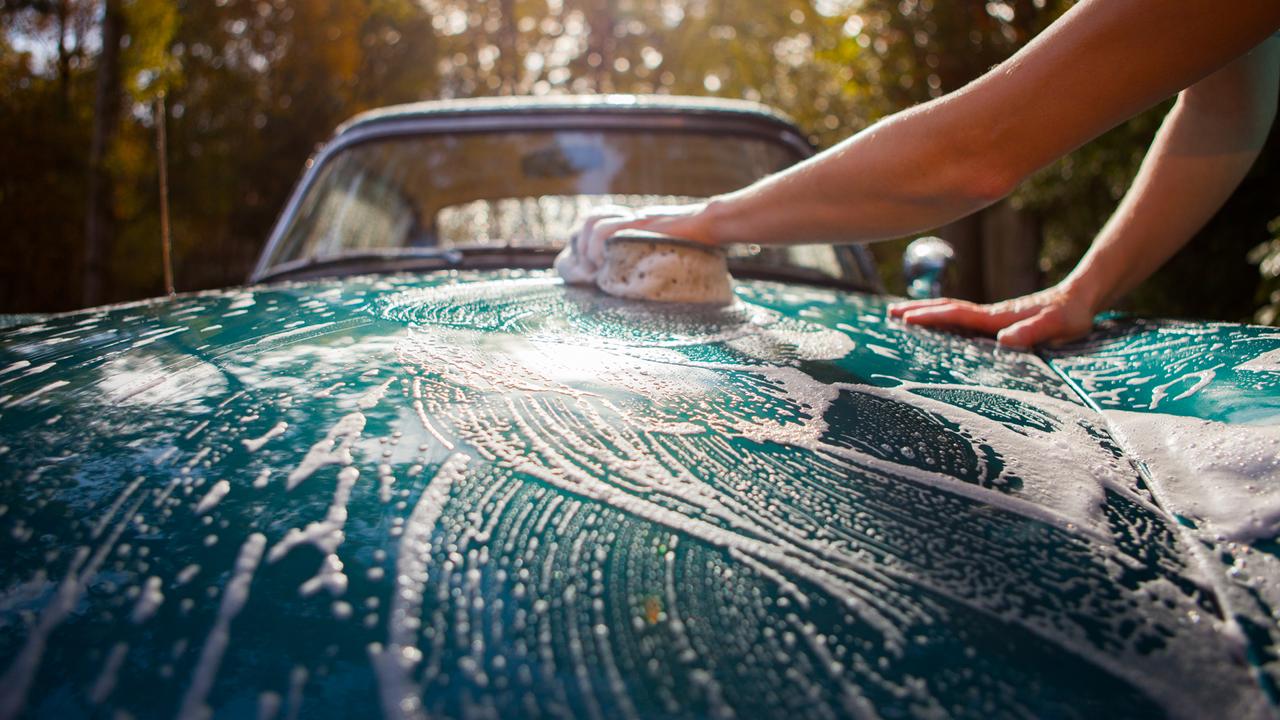 Young woman washing car at home in driveway.