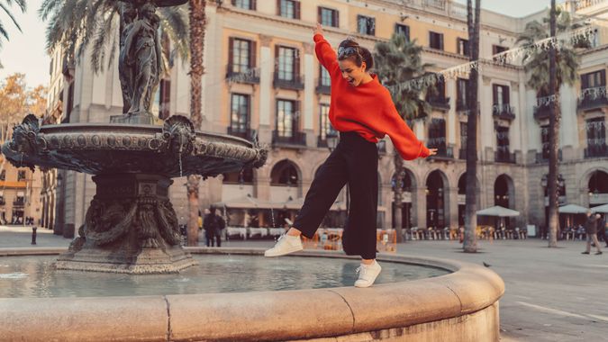 Smiling woman trying to keep balance while walking on one leg at the fountain.