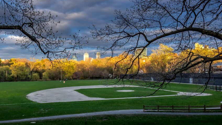Dusk falls on a little league field in Brookline, Massachusetts, with the towers of Boston in the background.