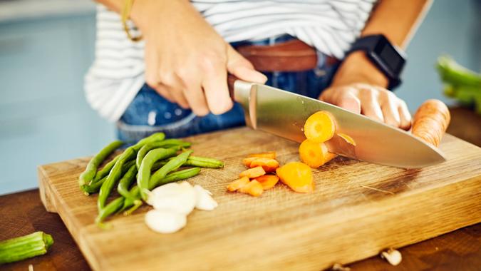 Close-up of woman cutting carrot on board.