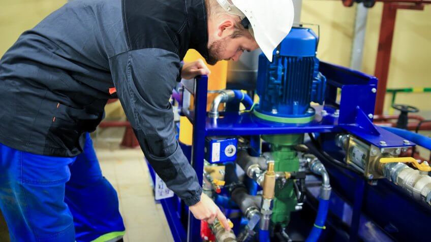Engineer checking oil pump and pressure gauge in industrial plant.