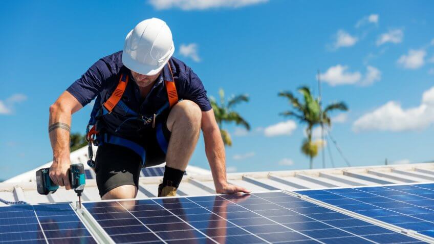Solar panel technician with drill installing solar panels on roof on a sunny day.