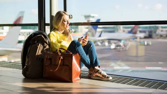 Woman sitting in airport and waiting for her flight, woman using phone in airport departure area.