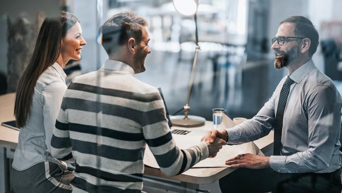 Happy real estate agent shaking hands with young couple after successful meeting in the office.