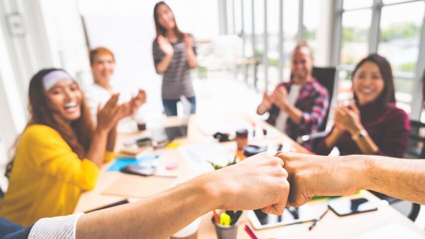 Business partners or coworkers fist bump in team meeting, multiethnic diverse group of happy colleagues clapping hands.