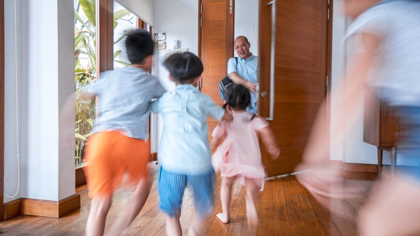 Father is hugging his children at the front door after coming home.