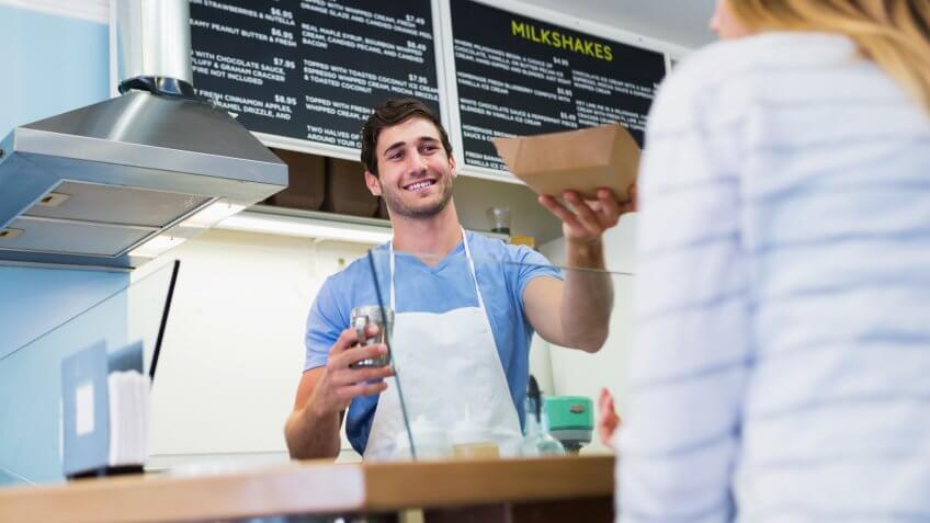 Young man (20s) working behind the counter of a shop selling gourmet waffles.