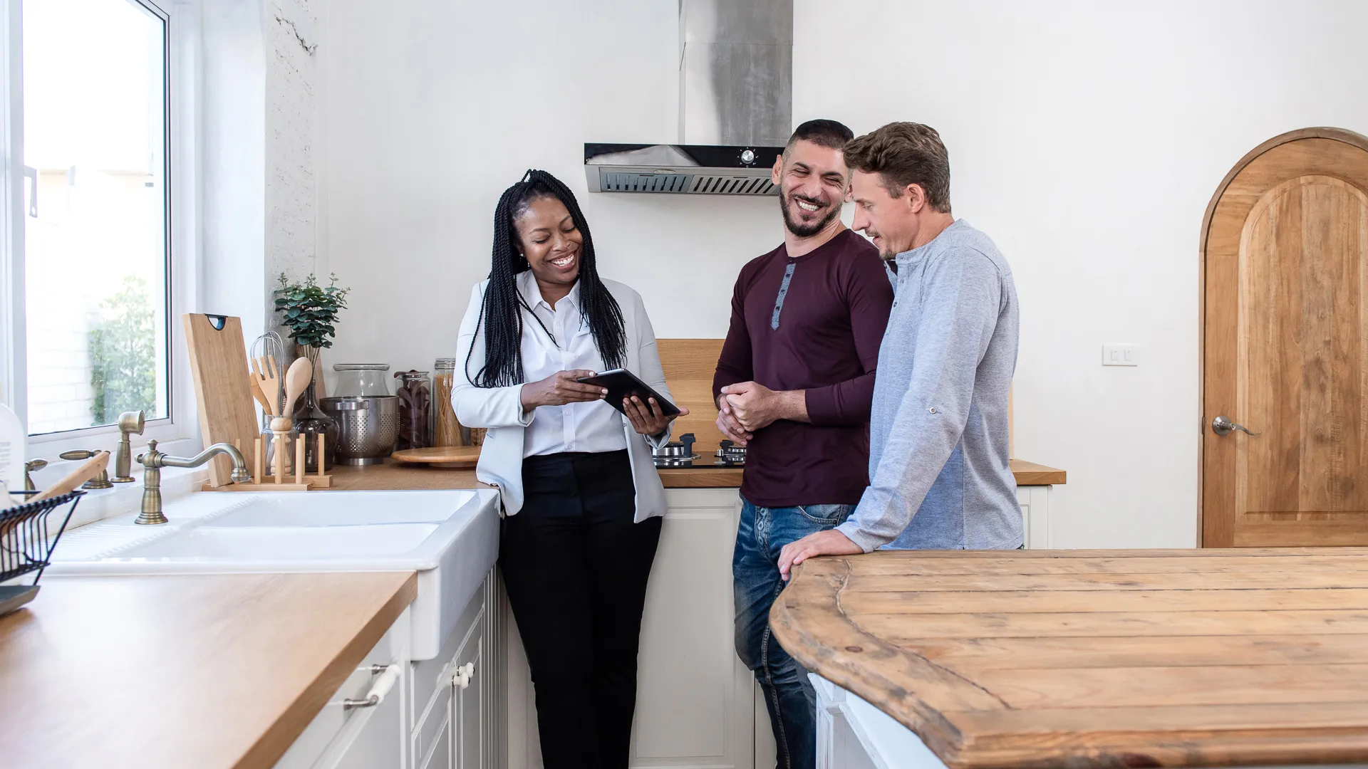 African american female real estate agent in kitchen showing gay couple around new house.
