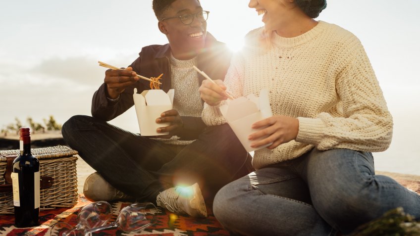 couple on picnic eating noodles and smiling on a sunny day.
