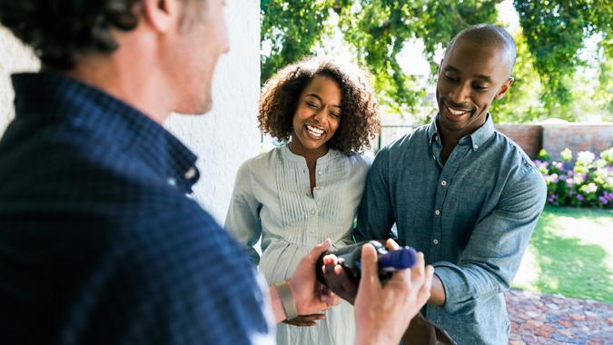 Happy couple giving wine bottle to man at home Happy couple giving wine bottle to man.