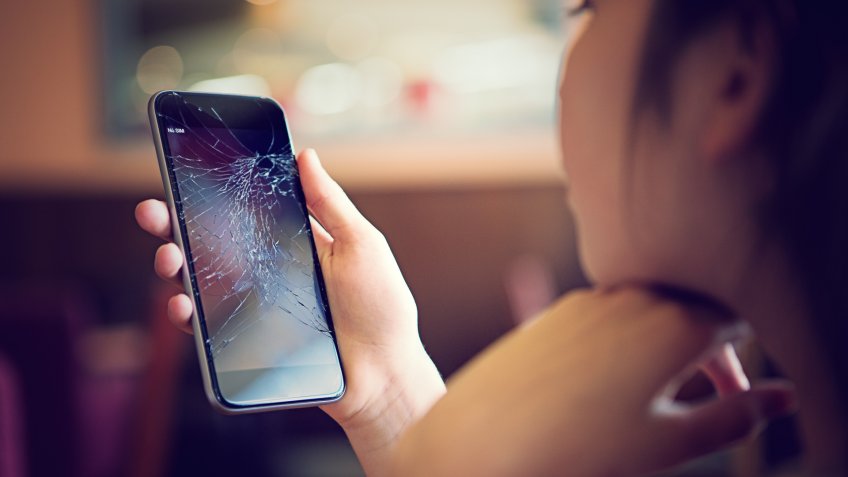 Young girl is watching her broken mobile phone after falling down.